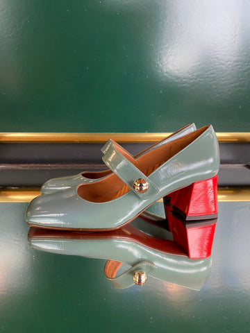 High-heeled shoes with red soles and light green/blue straps on a reflective surface
