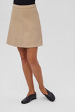 Woman wearing beige skirt and black leather shoes standing on a white background.