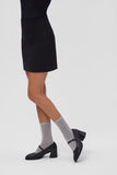 Woman wearing a black skirt, gray socks, and black Mary Jane shoes on a white background