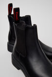 Black Chelsea boots with red branding on a light gray background