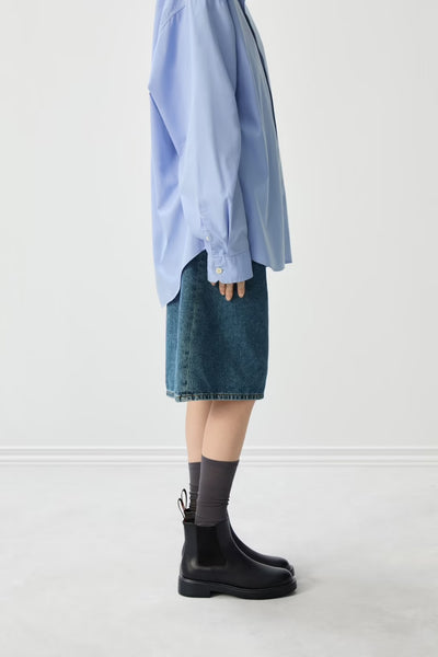 Close-up of black ankle boots worn with a denim skirt on a white background