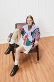 Woman sitting on a chair wearing a colorful plaid shirt and white skirt, styled with Camper Dean brown leather ankle boots from Kron in a bright room with wooden floors and white walls.