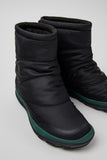 Pair of black winter boots with green accents on a light gray background