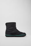 Black winter boot with green trim on a light gray background