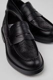 Close-up of black Camper Twins leather moccasins with brogue perforations, penny-loafer strap and rounded toe.