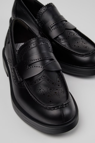 Close-up of black Camper Twins leather moccasins with brogue perforations, penny-loafer strap and rounded toe.