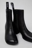 Close-up of Camper Kora black leather ankle boots showing the smooth leather upper and curved silhouette