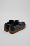 Rear three-quarter view of Camper Peu Terreno black leather moccasins showing the heel and brown rubber sole